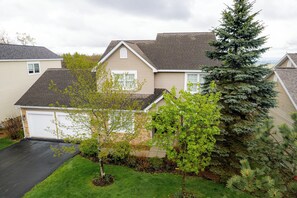 A residential house with a garage, a well-maintained lawn, and a large evergreen tree. - Mountain-View Home with Private Hot Tub, Game Room & Firepit — Sleeps 16 (Somerset)
