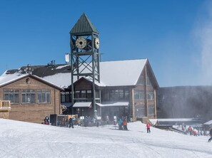 A ski resort with a prominent clock tower, wooden buildings, and a snowy landscape.