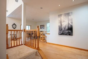 A spacious hallway with a wooden staircase, a dining area with wooden furniture, and a large wall-mounted artwork. - Mountain-View Home with Private Hot Tub, Game Room & Firepit — Sleeps 16 (Somerset)