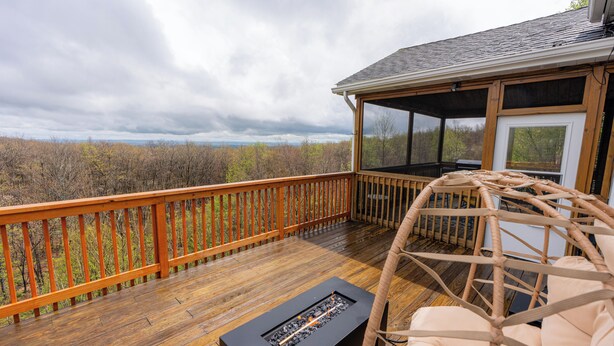 Une terrasse en bois avec un foyer et un fauteuil en osier, offrant une vue sur un paysage boisé.