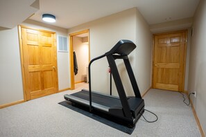 A home gym with a treadmill, carpeted floor, wooden doors, and a ceiling light.