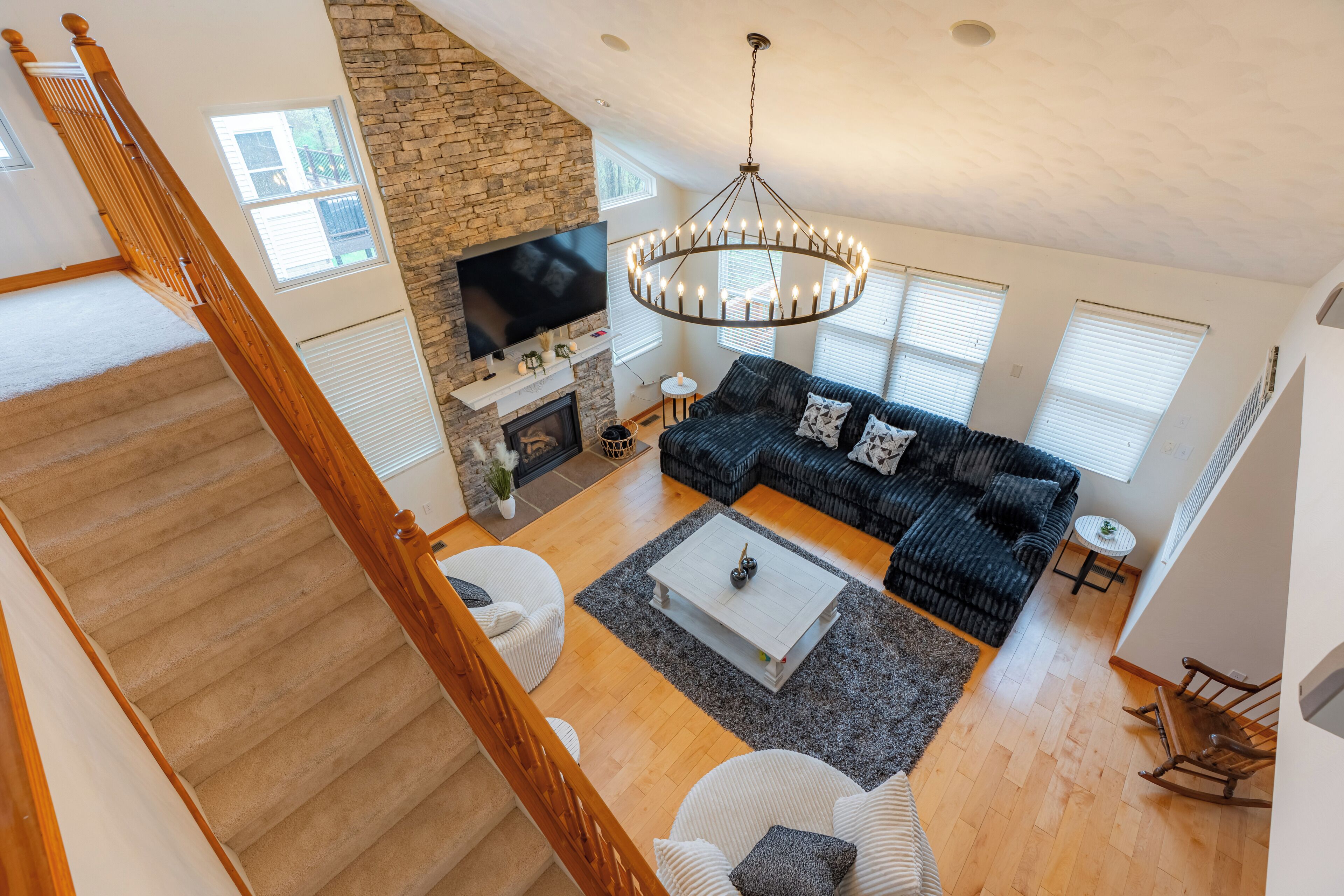 A spacious living room with a stone fireplace, a large TV, and a chandelier.