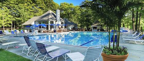 A swimming pool with lounge chairs and umbrellas, surrounded by trees and a building with a chimney.