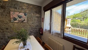 Een eethoek met een stenen muur, een tafel met een vaas vol groen, en een raam met uitzicht op een balkon en buitenplanten.