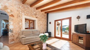 A living room with a stone wall, a sofa, a glass coffee table, and a television. - CAN LLIGANYA - Rustic villa with private pool and free wifi (Felanitx)