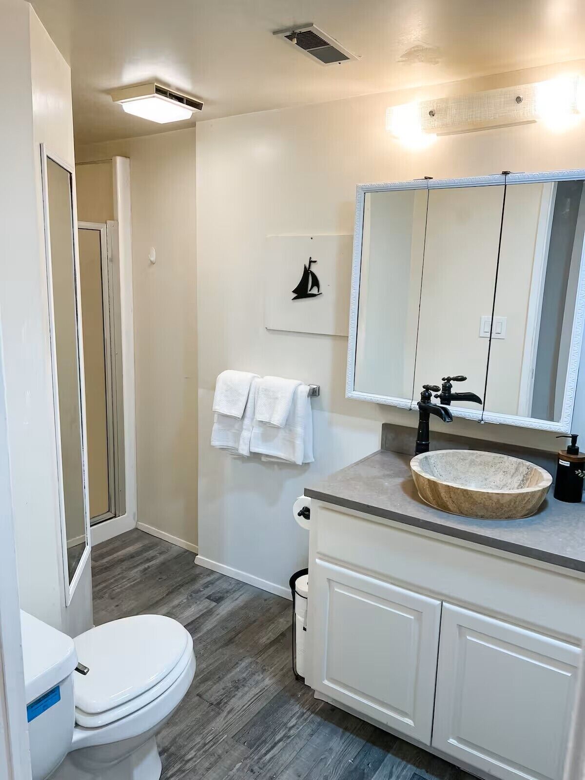 Un baño con inodoro blanco, lavabo de mármol, espejo y un perchero para toallas.