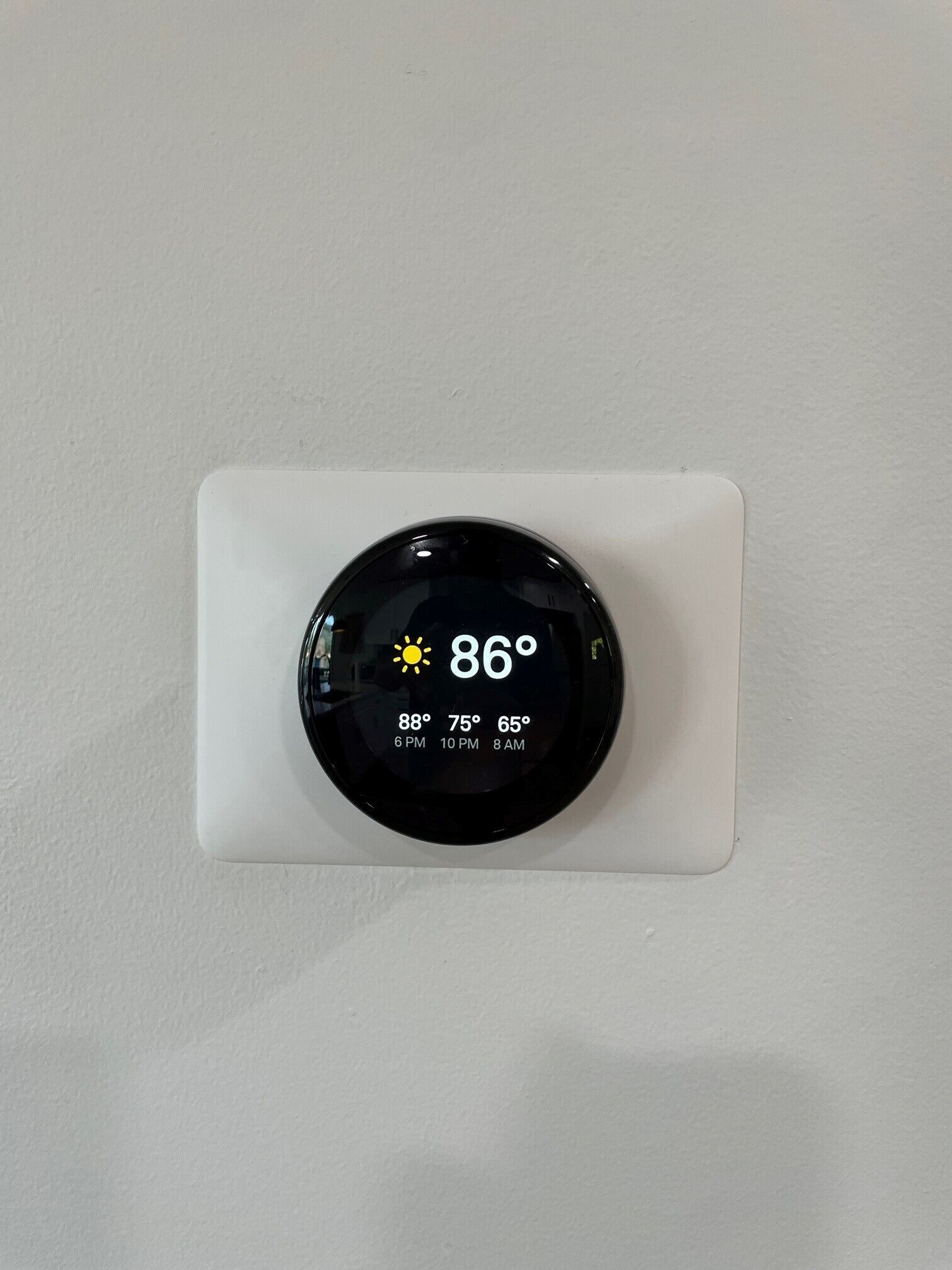 Termostato montado en una pared blanca que muestra una temperatura actual de 86 grados.