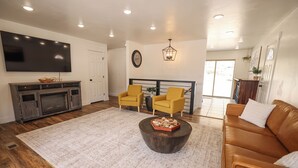 A modern living room with a flat-screen TV, a wooden coffee table, a brown leather sofa, and yellow chairs. - Entire House Between Zion & Bryce w/ Hot Tub! (Orderville)