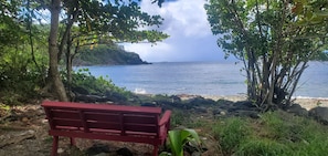 A red bench overlooking a rocky shoreline with a view of the ocean and a distant building on a cliff.