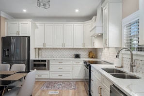 A modern kitchen with white cabinetry, stainless steel appliances, and a dining area with a table and chairs.