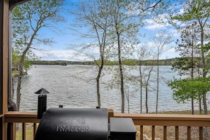 Une vue depuis une terrasse donnant sur un lac bordé d’arbres, avec un barbecue portant l’inscription « TRAEGER », et une rive lointaine.