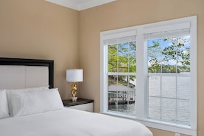 A hotel room with a bed, a nightstand with a lamp, and a large window with a view of a dock and greenery.