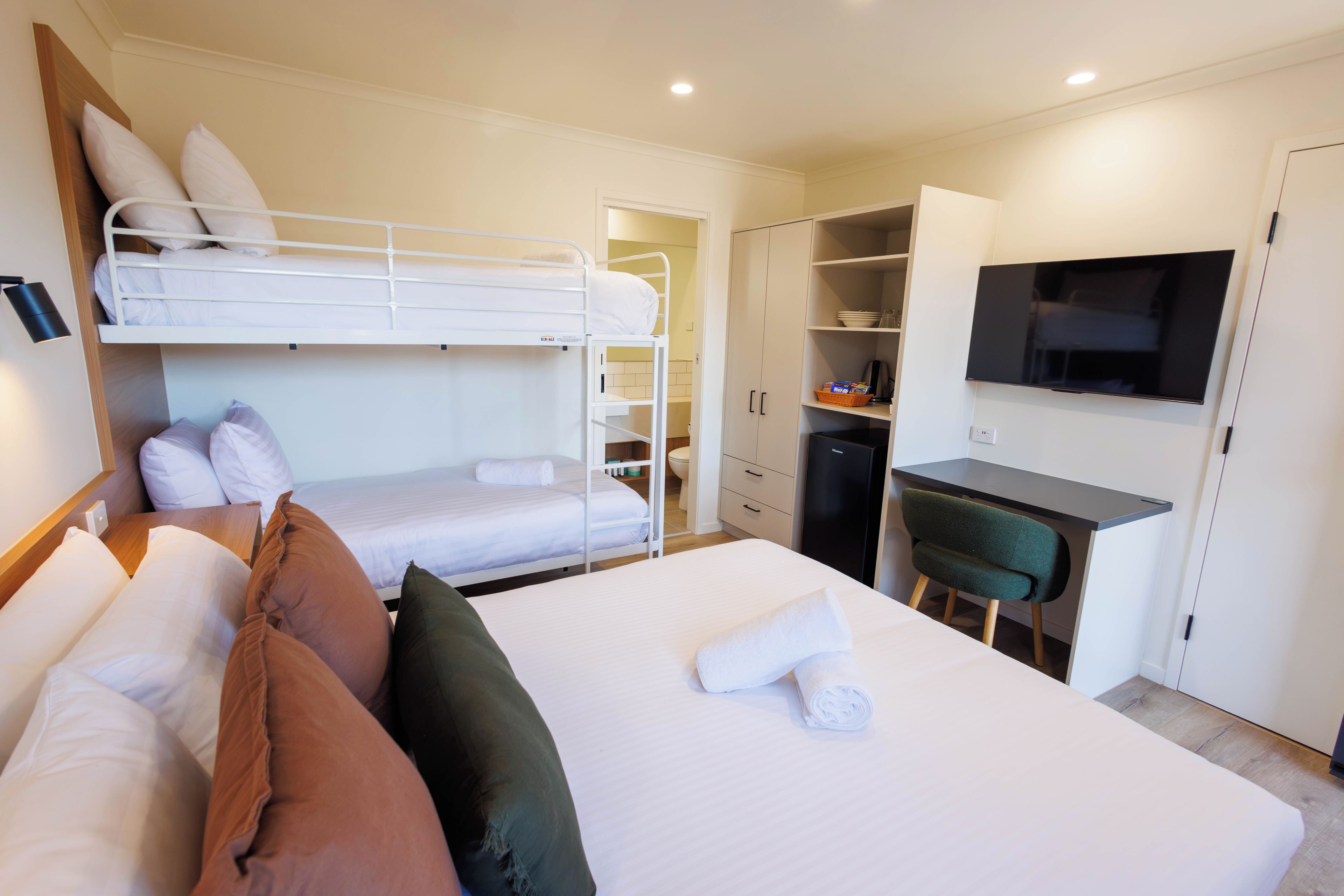 Una habitación de hotel con literas, un escritorio, una silla, un televisor y un armario.