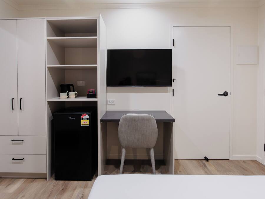 A bedroom with a bed, a desk with a chair, a television, a refrigerator, and a wardrobe.