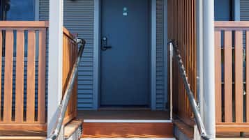 Un conjunto de escaleras de madera que conducen a una puerta azul con una placa de números, flanqueadas por barandas de madera y pasamanos metálicos.