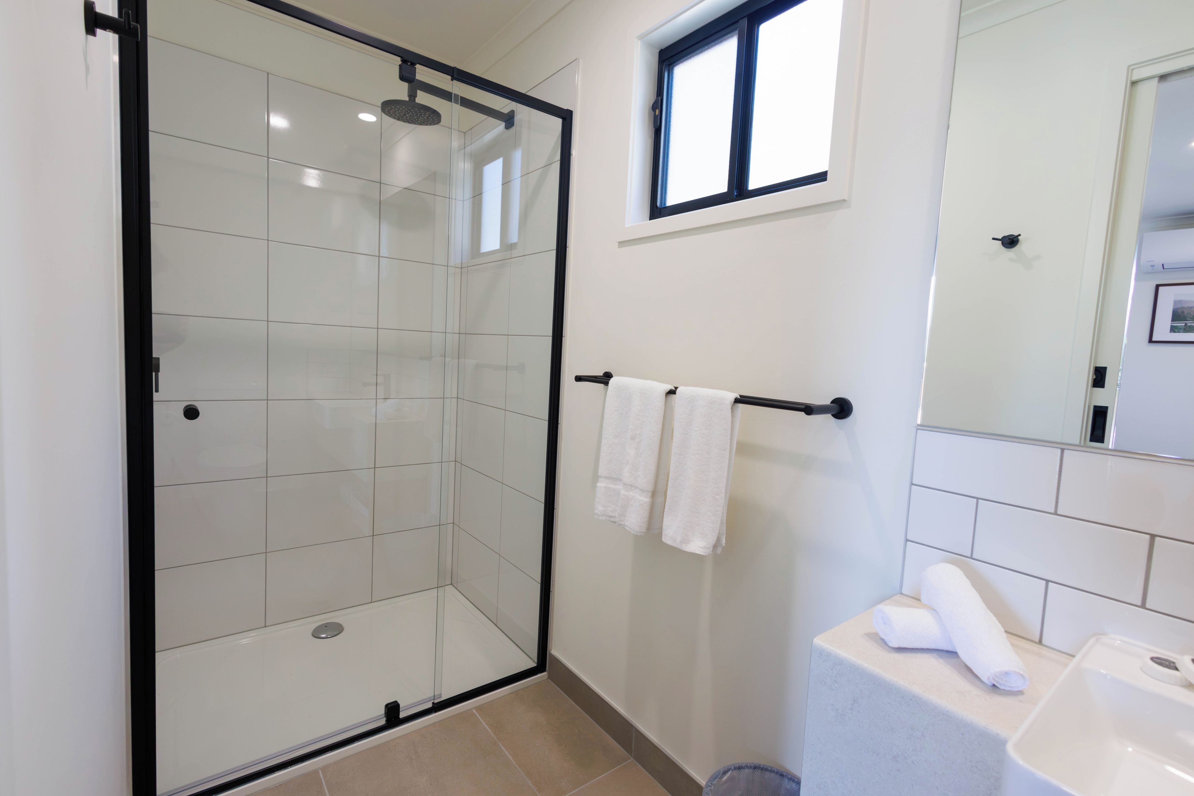 Une salle de bain moderne avec une douche à parois de verre, un porte-serviettes avec deux serviettes et un lavabo avec un miroir.