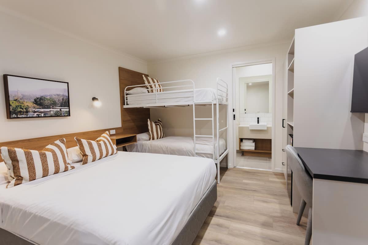 A hotel room with a bunk bed, a desk, and a bathroom.