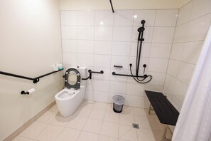 A standard bathroom with a toilet, a shower, and a bench. - Coomera Lodge Hotel (Oxenford)