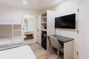 Uma cama beliche, uma escrivaninha com cadeira, uma televisão e um guarda-roupa num quarto.