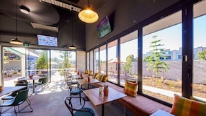 An indoor seating area with tables and chairs, large windows, and a TV screen. - Coomera Lodge Hotel (Oxenford)