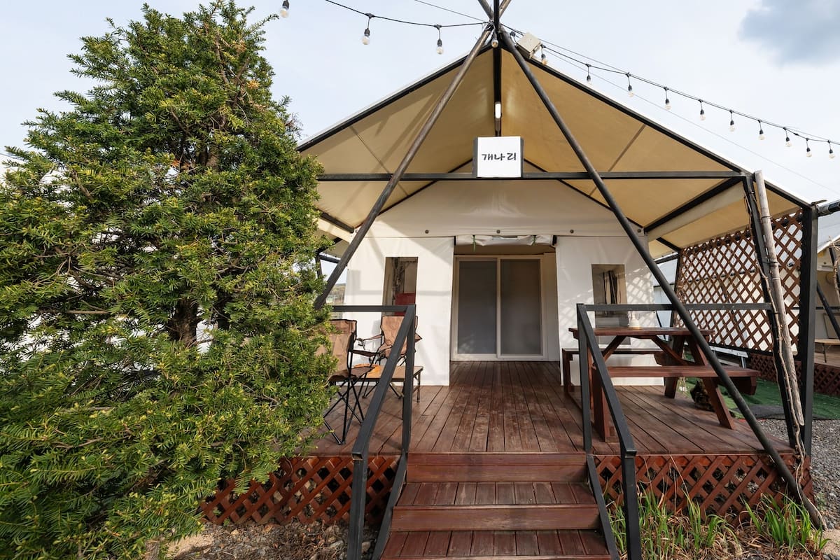 A tented accommodation with a wooden deck, a sign indicating the name, and a view of the surrounding area.