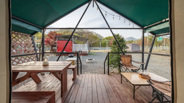 A covered outdoor seating area with wooden tables and chairs, a fire pit, and a view of the surrounding landscape. - Chaesonghwa Glamping in Yeongcheon (Yeongcheon)