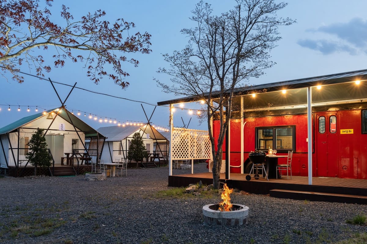 A red bus converted into a restaurant with a fire pit in front.