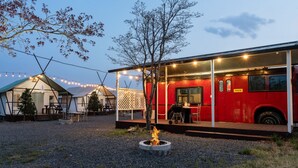 Un autobus rouge transformé en restaurant, avec un foyer installé à l’avant.