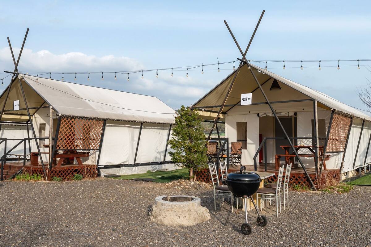 Two tents with a barbecue grill and a fire pit in front.