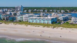 A beachfront hotel with multiple balconies, a sandy beach, and a view of the ocean. - A Place At The Beach #1D by Carolina Retreats (Carolina Beach)