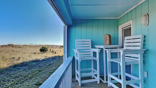 A porch with two white chairs and a table, overlooking a grassy field. - A Place At The Beach #1D by Carolina Retreats (Carolina Beach)