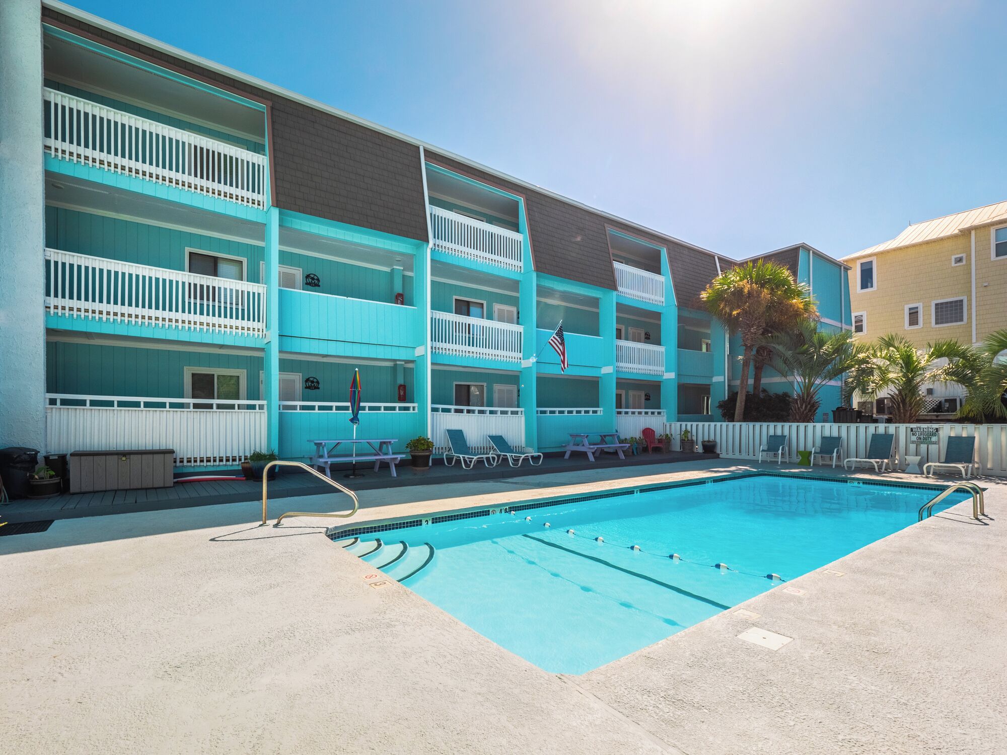 A multi-story hotel with a pool area, including lounge chairs and a flag.
