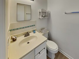 Un baño con lavamanos, espejo, inodoro y un pequeño estante con artículos de aseo.