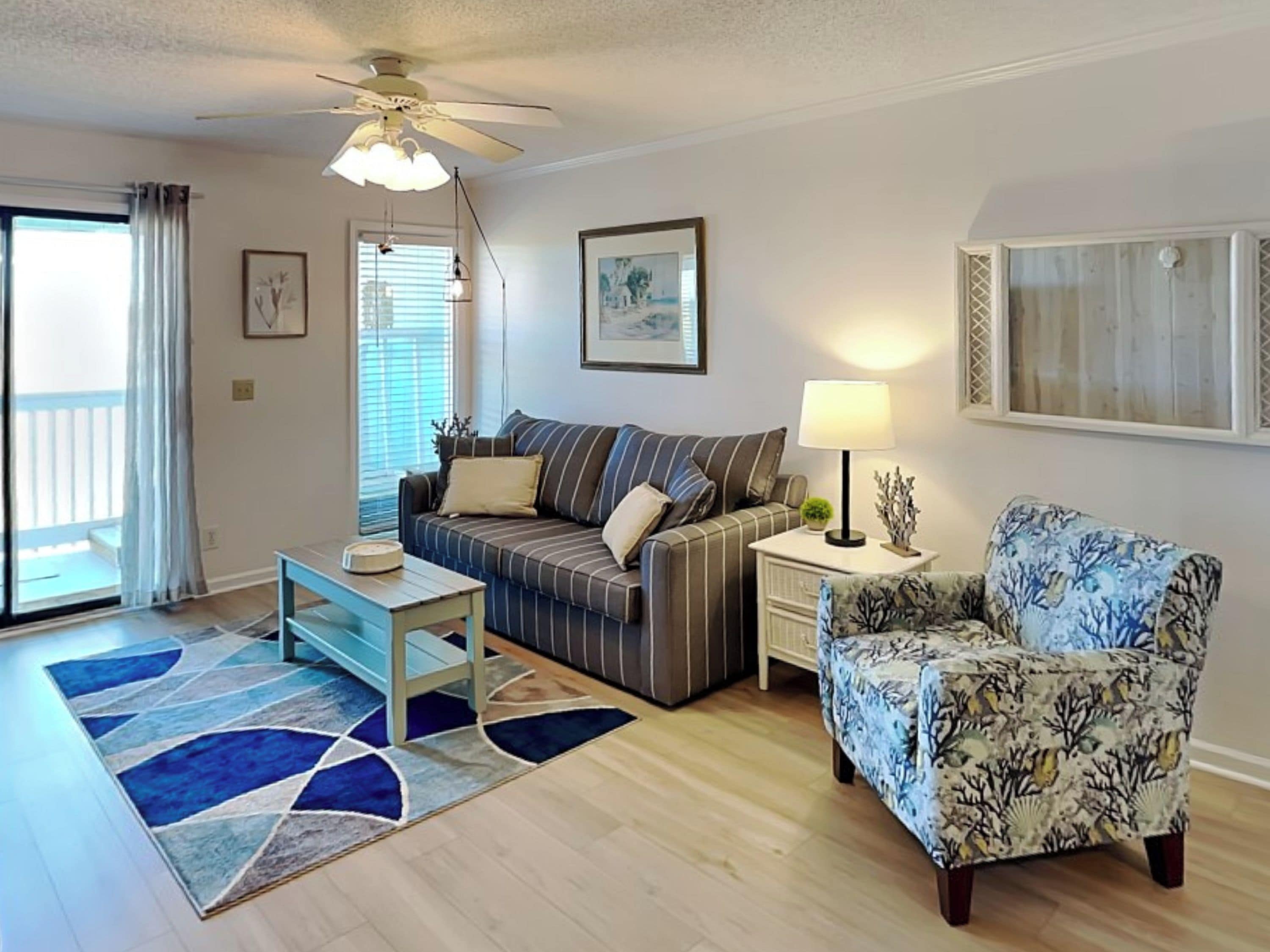 A living room with a sofa, a patterned armchair, a coffee table, a lamp, and a ceiling fan.