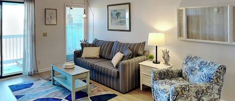 A living room with a sofa, a patterned armchair, a coffee table, a lamp, and a ceiling fan.