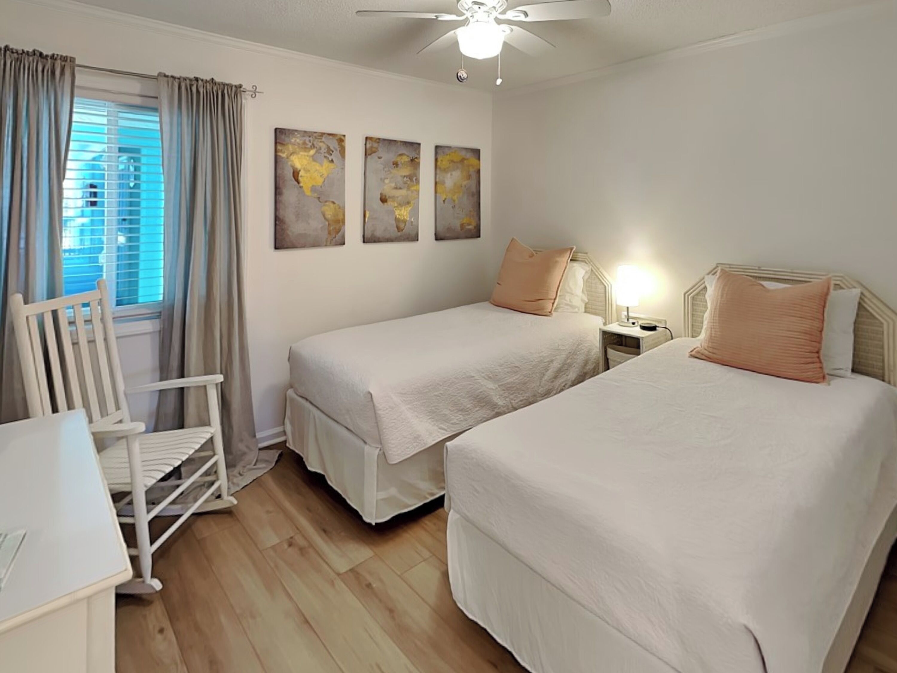 Une chambre avec deux lits simples, un bureau, une chaise et un ventilateur de plafond.