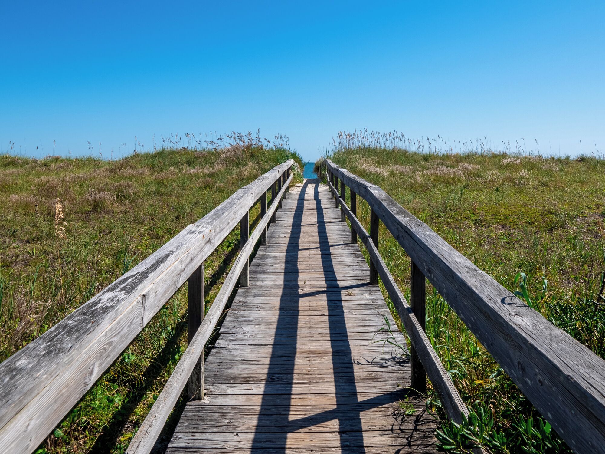 A wooden boardwalk leading to a distant point, surrounded by grassy fields.