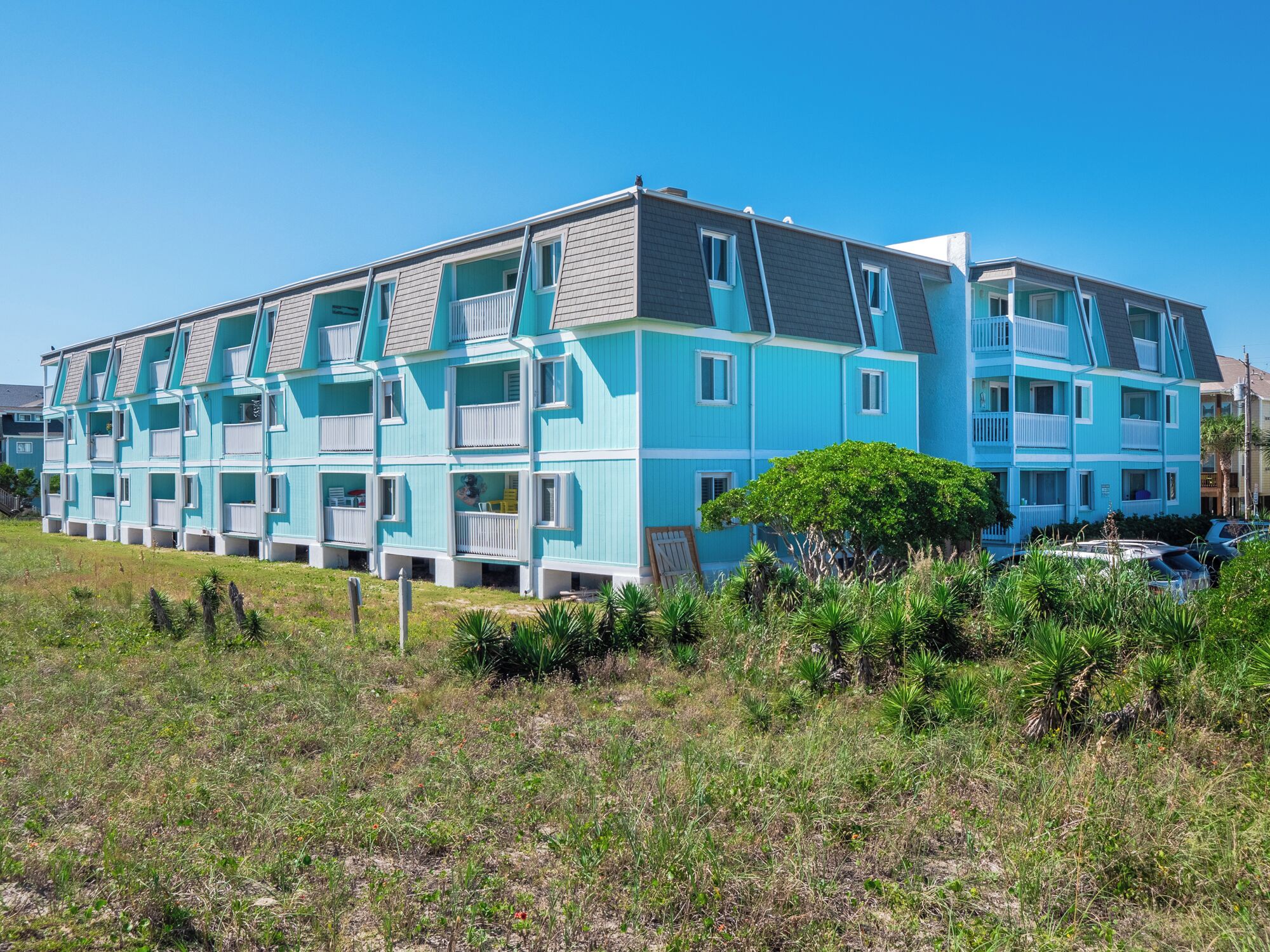 A multi-story residential building with balconies, a flat roof, and a grassy foreground.