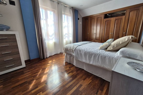 A bedroom with a wooden wardrobe, a bed with pillows, and a dresser.