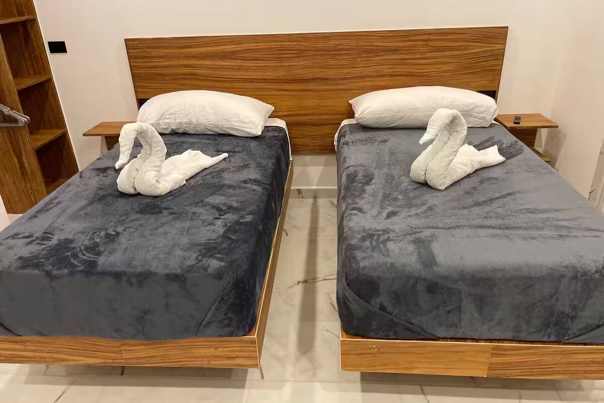 Two beds with dark grey bedding and wooden headboards.