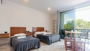 Una moderna camera d'albergo con due letti, un balcone con tavolo e sedie, e un'ampia finestra che offre vista sul verde.