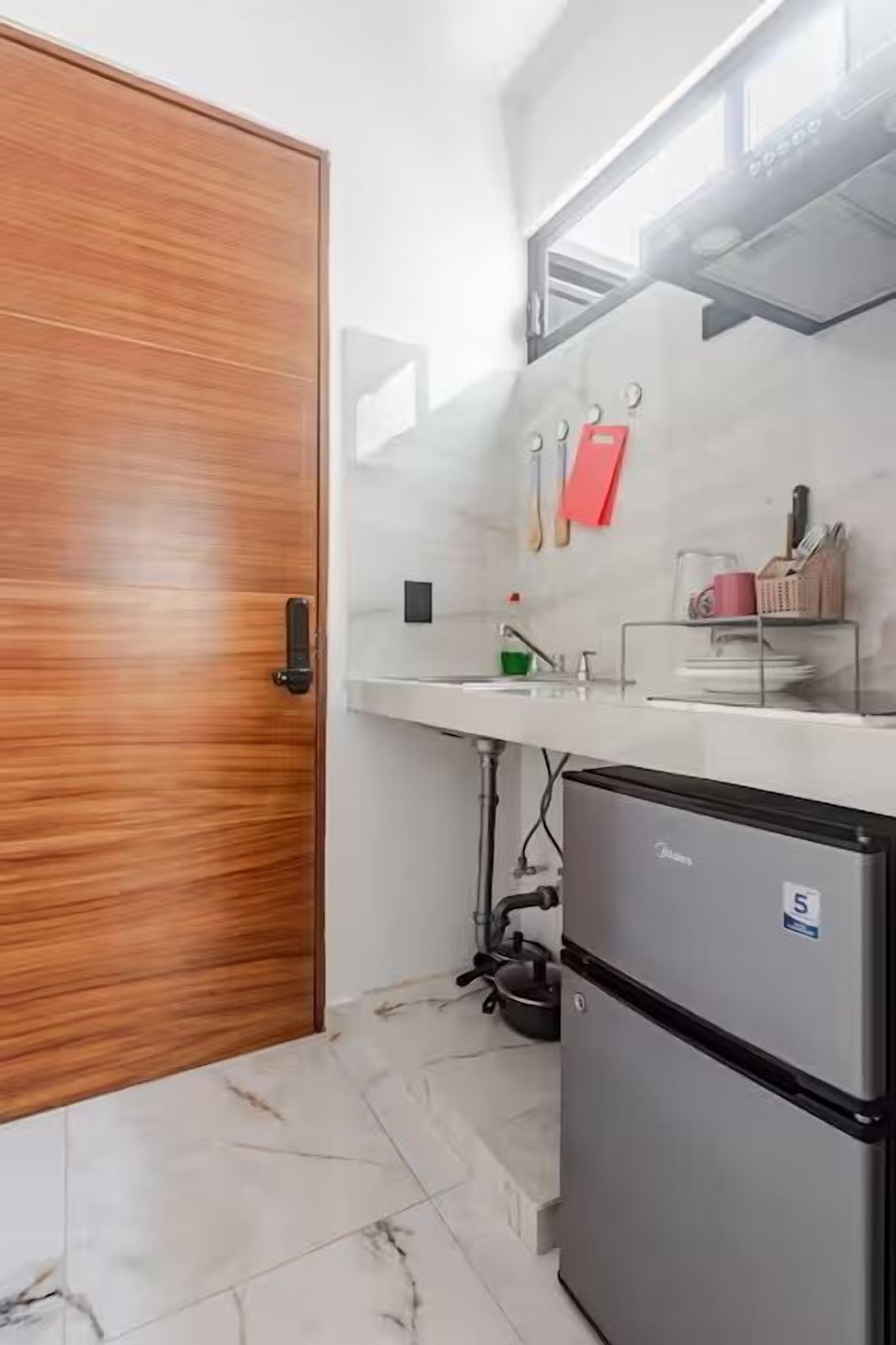 A compact kitchen with a wooden door, a small refrigerator, a white countertop, and a sink.