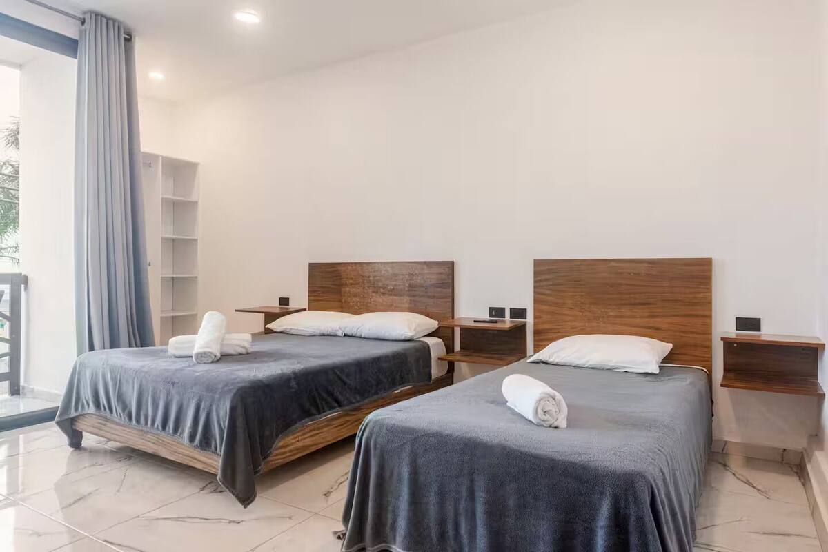 A hotel room with two beds, each with a wooden headboard, a small bedside table, and a shelf.