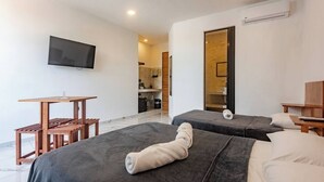 Una camera d'albergo con due letti, una televisione, un piccolo tavolo di legno e una angolo cottura sullo sfondo.
