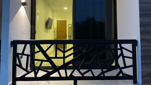 Un balcone moderno con ringhiera geometrica, una porta vetrata che dà su un ambiente interno e un televisore piatto a parete.
