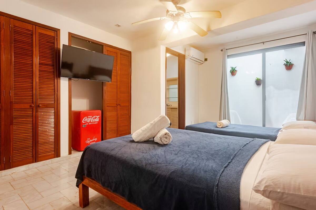 A hotel room with two beds, wooden wardrobes, a television, an air conditioning unit, and a window with curtains.