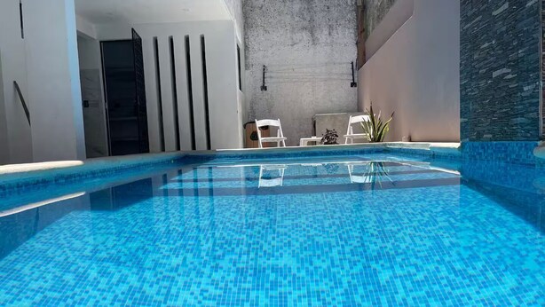 Una piscina interna con acqua cristallina, poltrone da relax bianche e una parete in pietra.