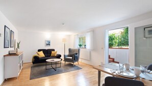 A modern living room with a sofa, armchair, coffee table, and dining table with chairs. - Lake Constance Bungalow – 'Souterrain' Apartment with Private Terrace, Shared Garden & Wi-Fi (Immenstaad am Bodensee)