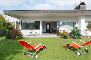A modern house with a patio, two sun loungers, and a dining area. - Lake Constance Bungalow – 'Souterrain' Apartment with Private Terrace, Shared Garden & Wi-Fi (Immenstaad am Bodensee)