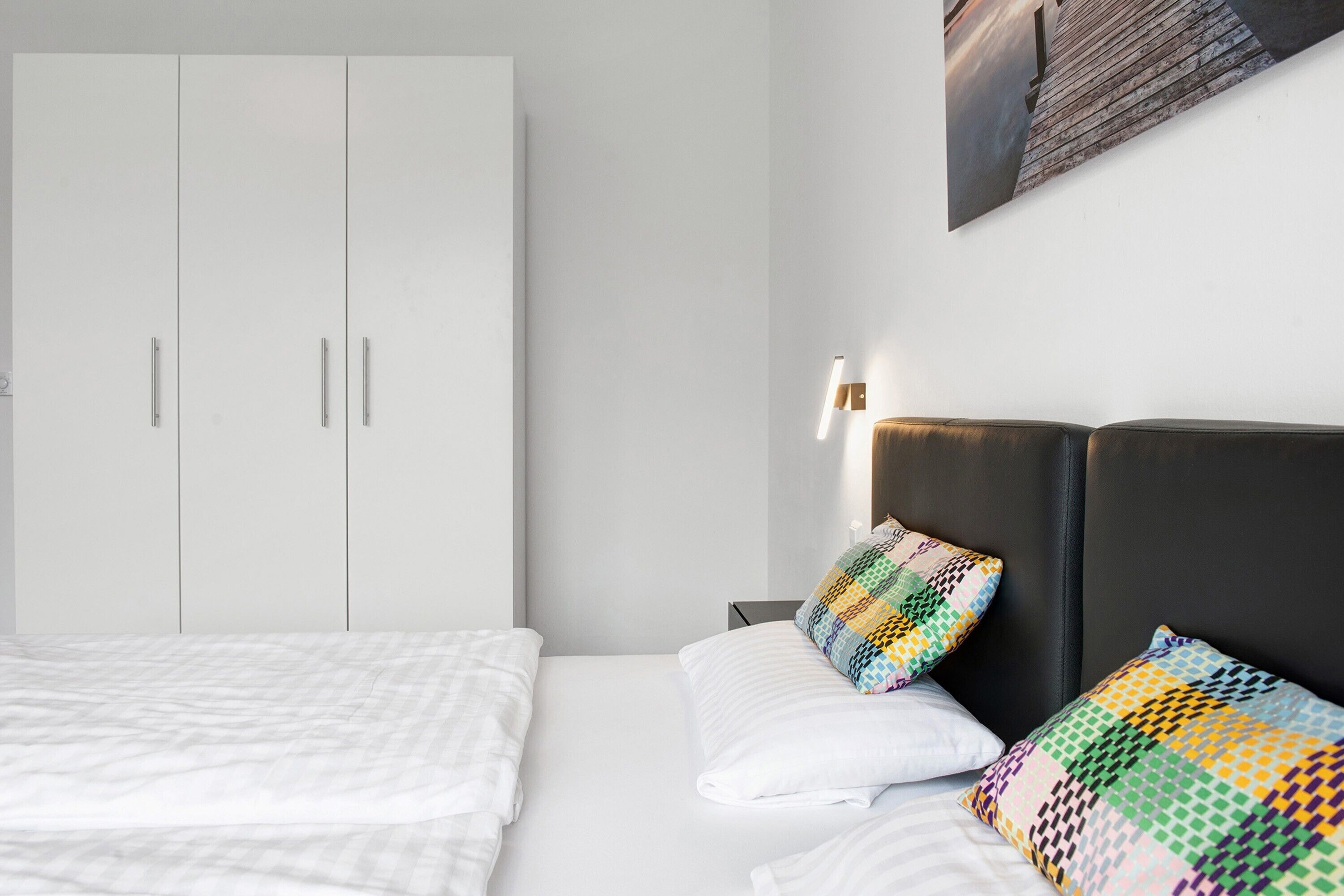 Quarto de hotel com cama, guarda-roupa, mesa de cabeceira e luminária na parede.